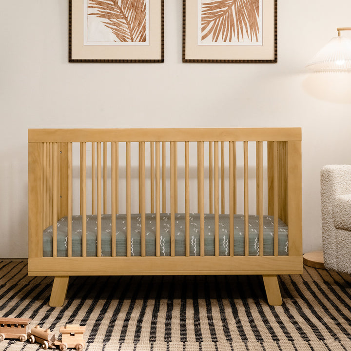 Front view of Babyletto Hudson 3-in-1 Convertible Crib And Toddler Rail next to recliner in -- Color_Honey