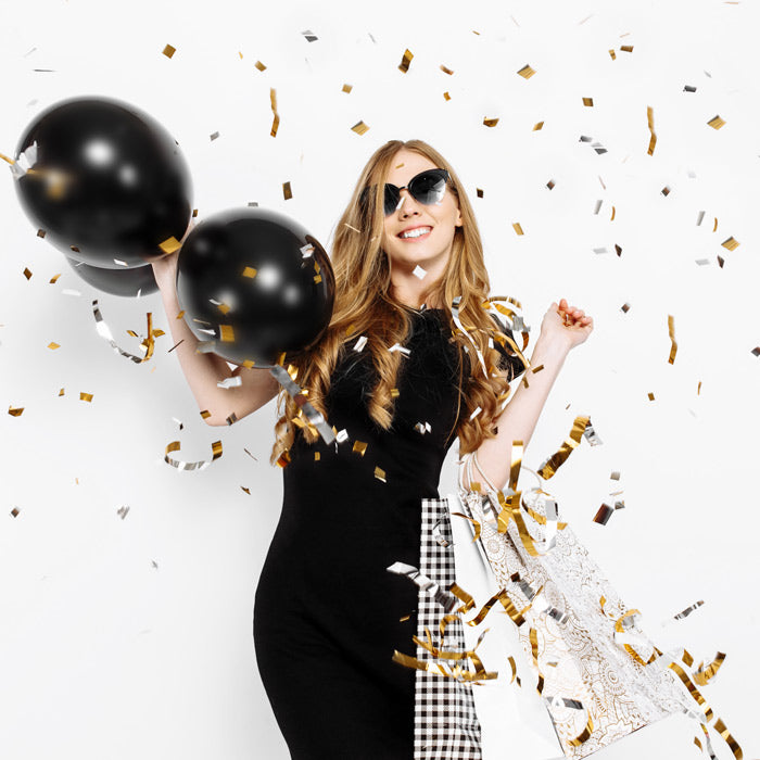 woman holding shopping bags and balloons surrounded by gold confetti
