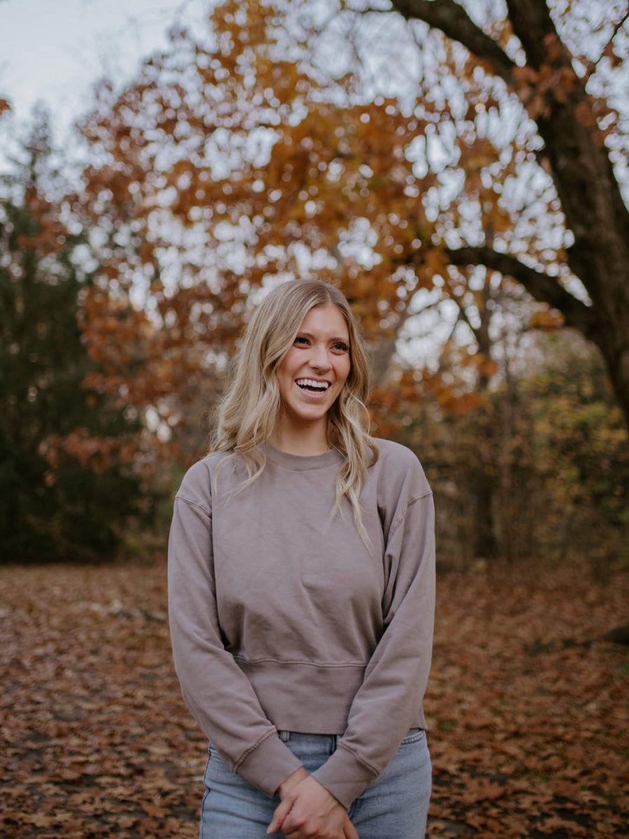 woman standing in autumn leaves with sweater and jeans smiling