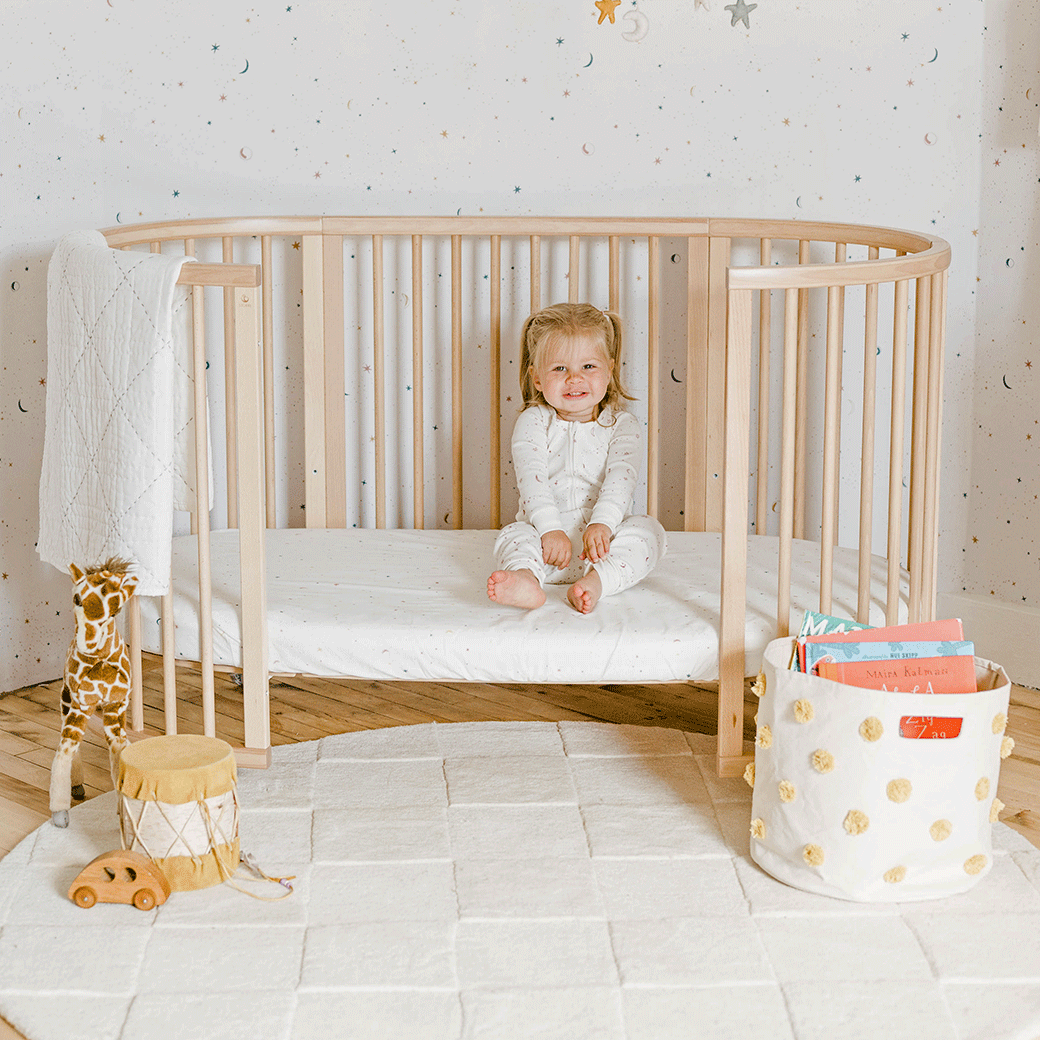 A baby in a toddler bed sitting on a Stokke's Sleepi V3 Fitted Sheet By Pehr in -- Color_Celestial